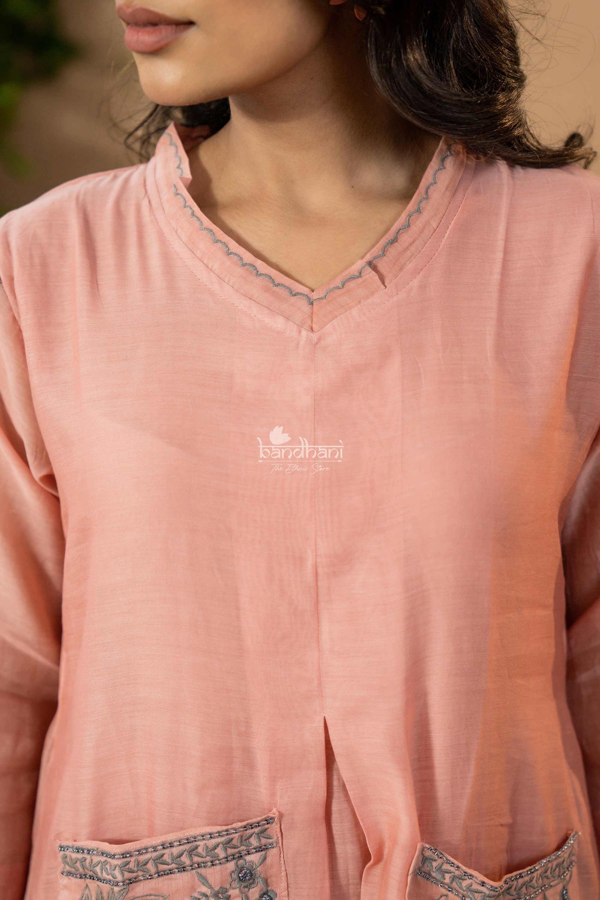 Close-up of a pink kurta with lace details and a brand logo.