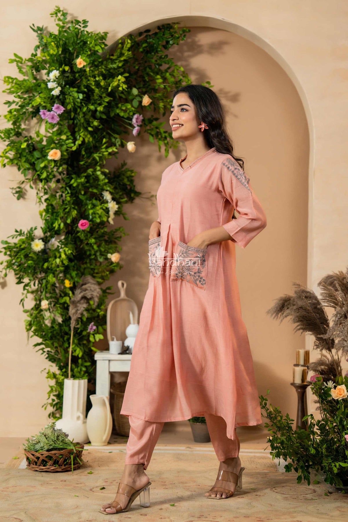 Woman in a pink dress standing in a decorated indoor setting with plants and flowers.