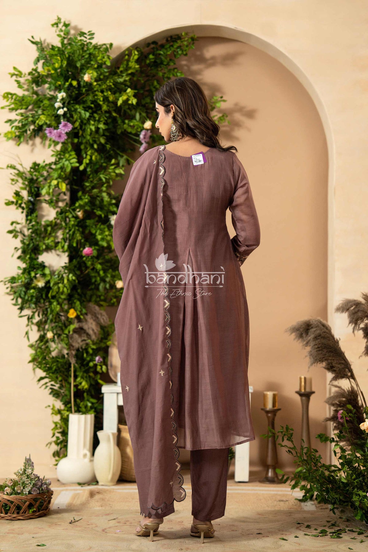 Woman wearing a mauve outfit with a decorative arch and plants in the background