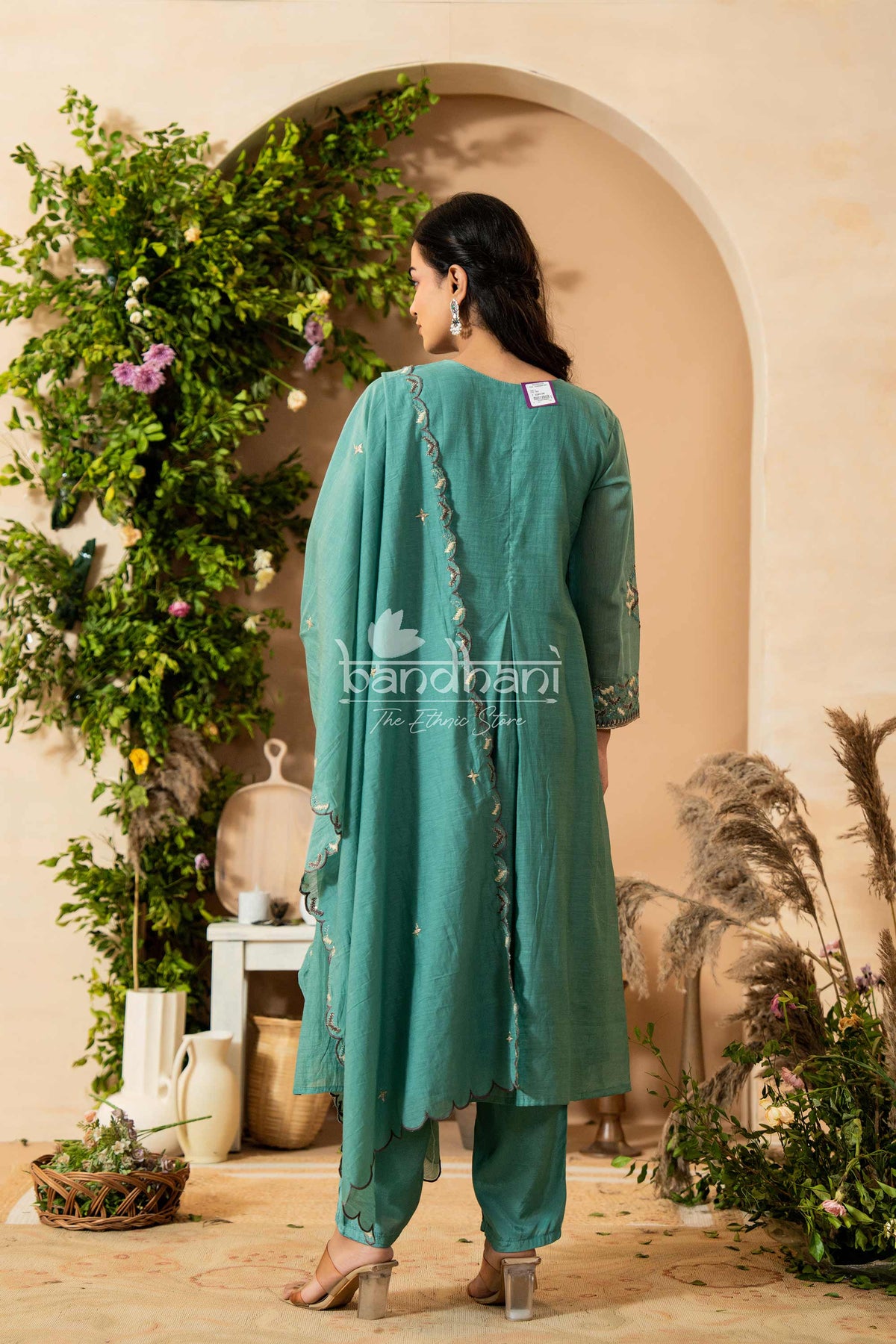 Woman in a teal outfit standing in front of a decorated archway with plants.