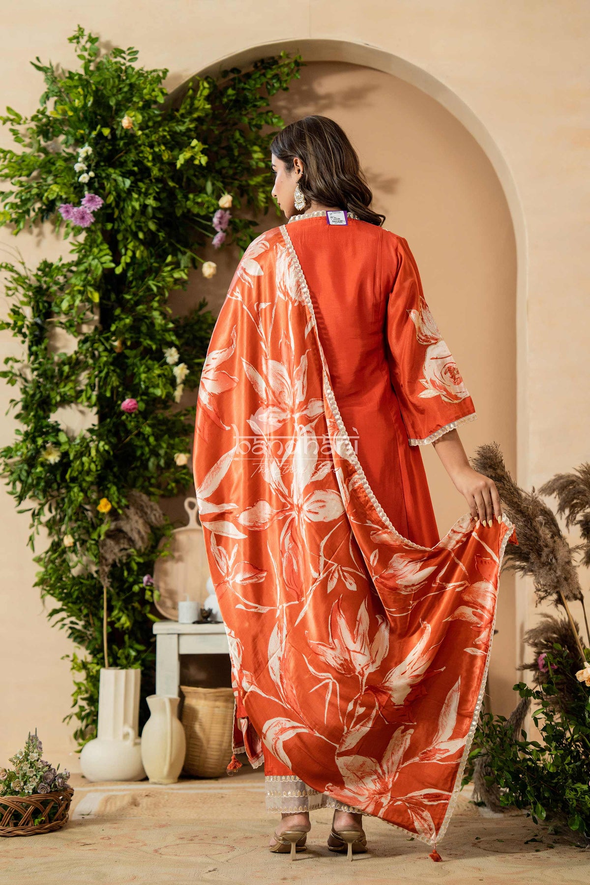 Woman in a red floral dress standing in a decorative indoor setting with plants and vases.