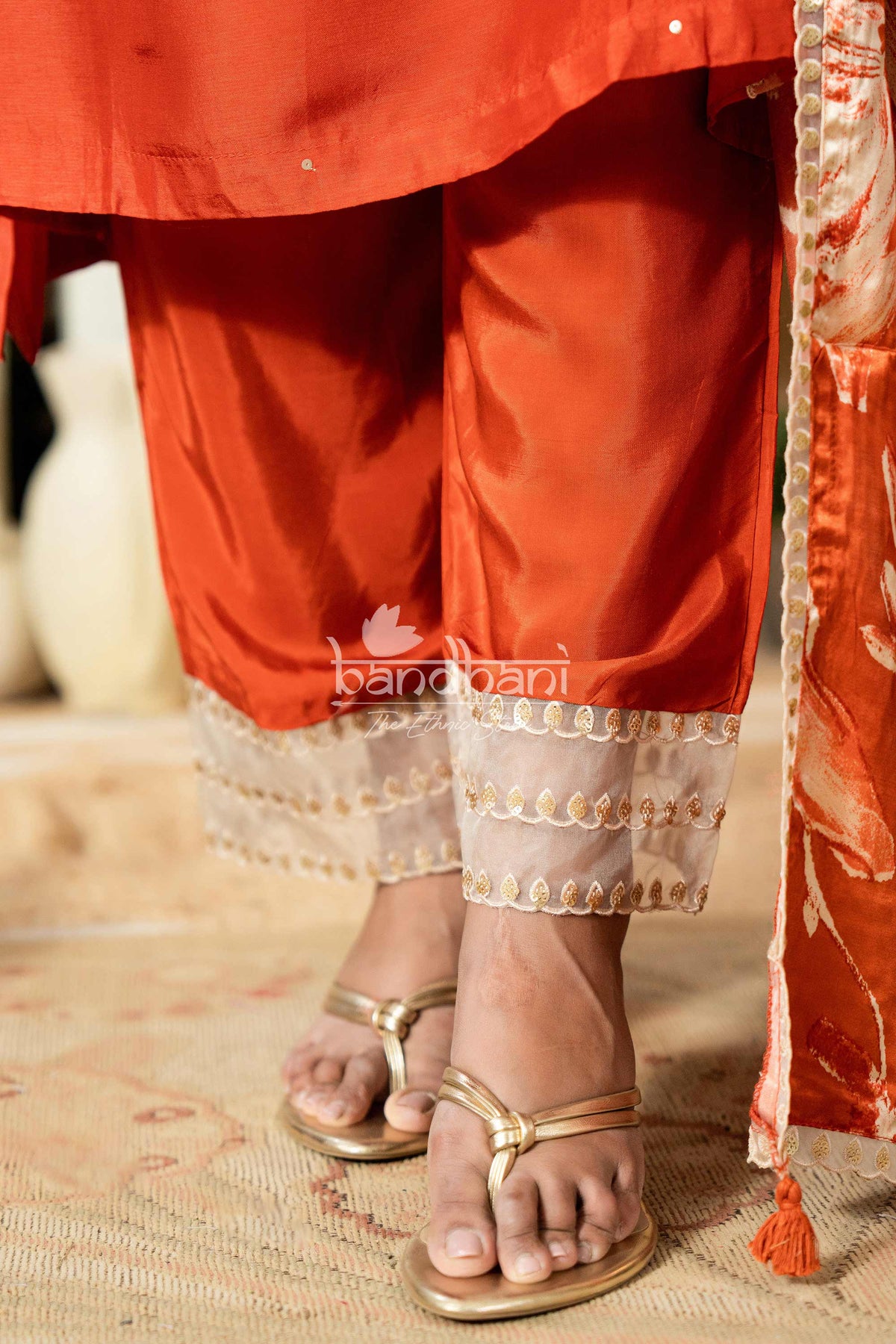 Close-up of red traditional outfit with gold sandals on a textured surface