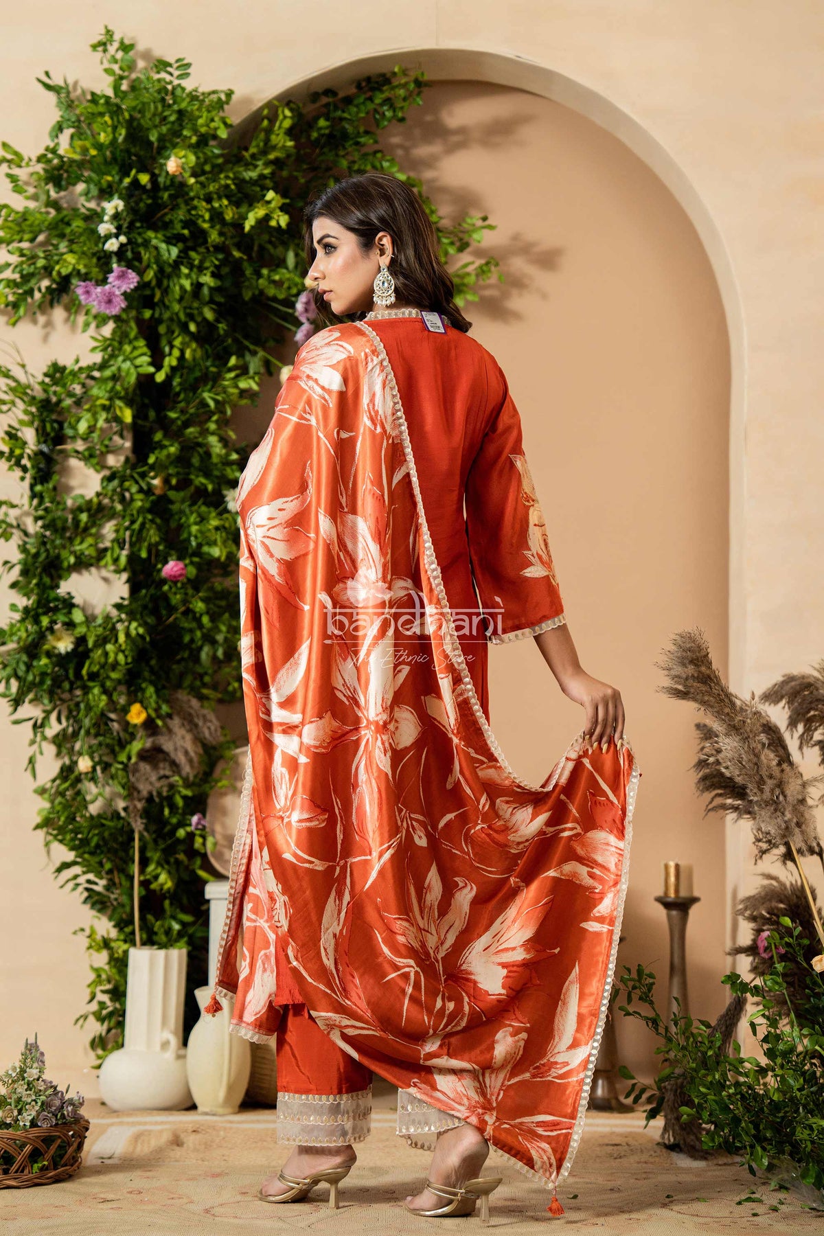 Woman in an orange and white traditional outfit standing in a decorated outdoor setting.