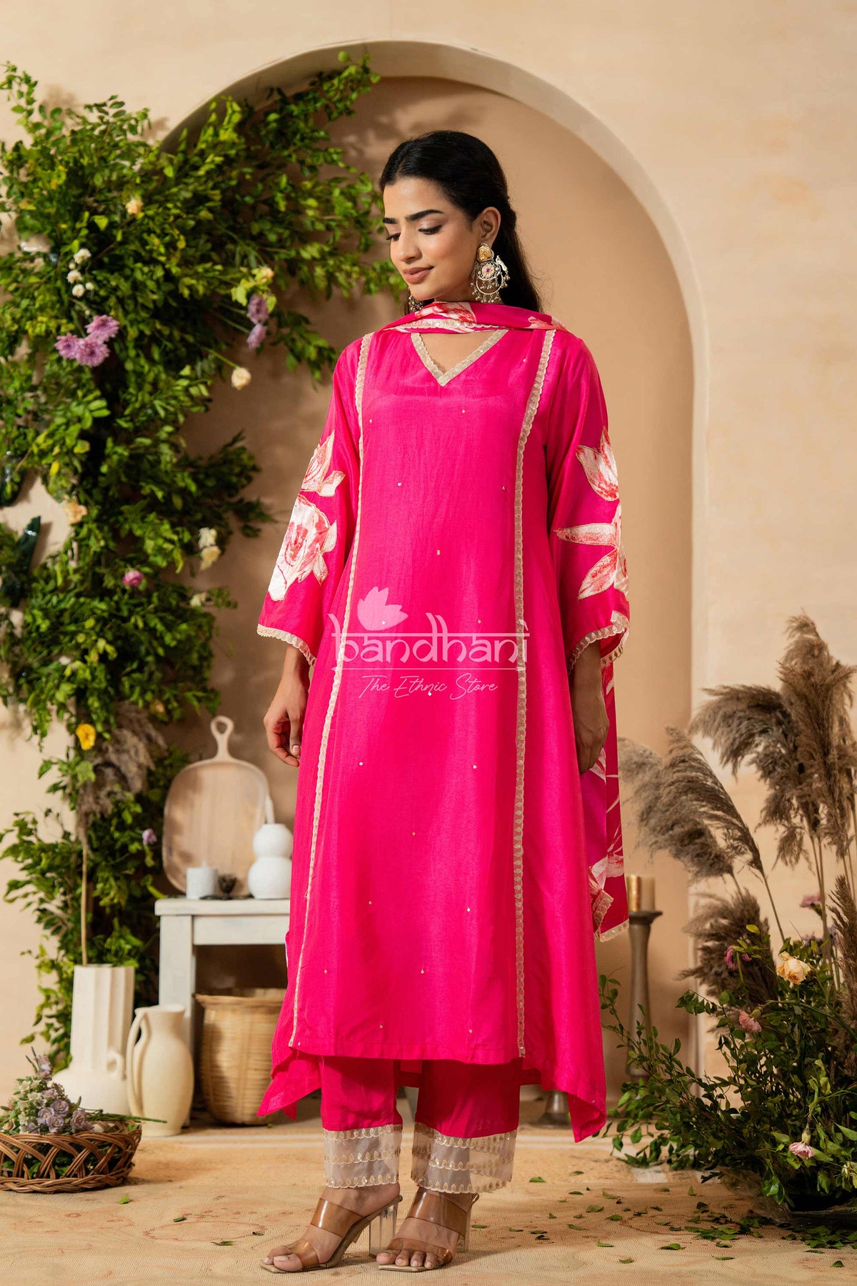 Woman in a bright pink traditional outfit with floral patterns standing in a decorative setting.