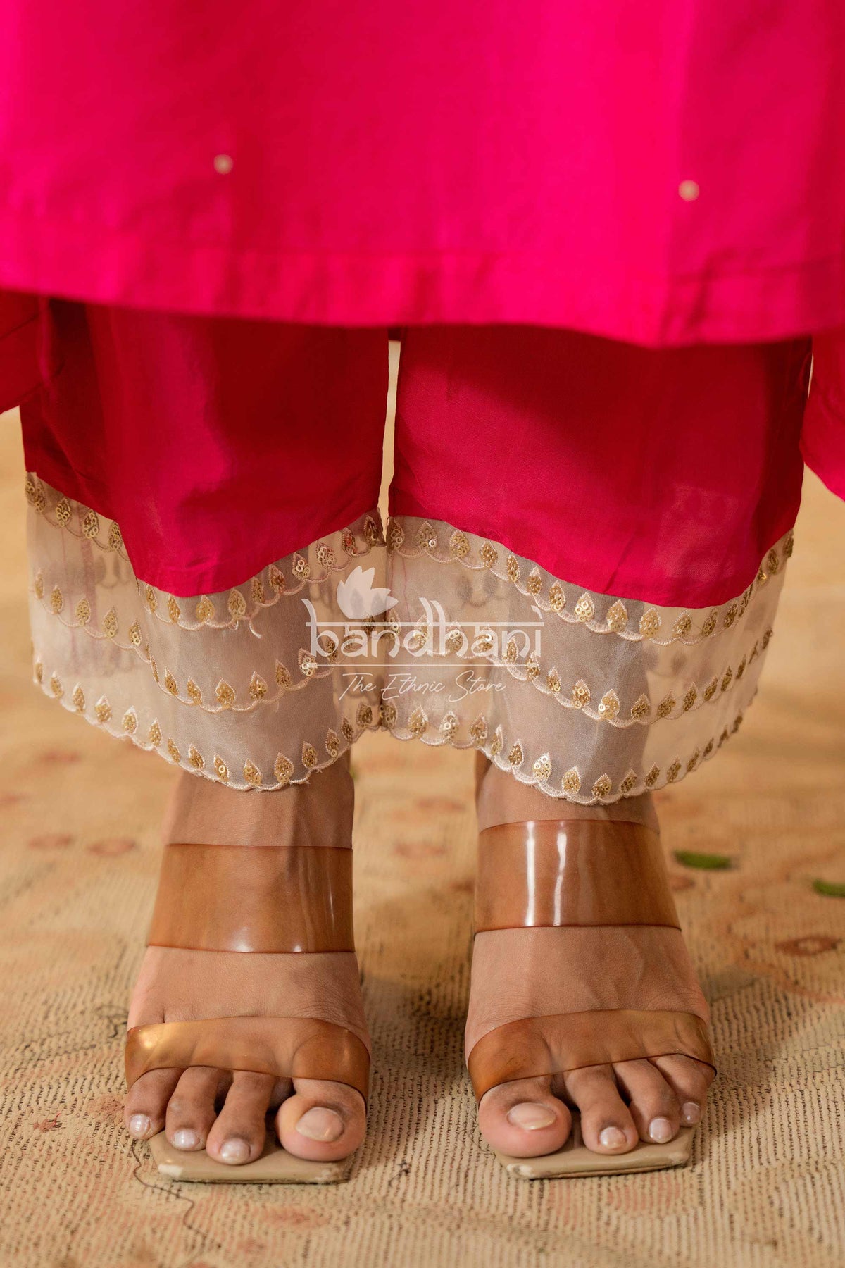 Person wearing a bright pink traditional outfit with a gold border, standing on a textured surface.