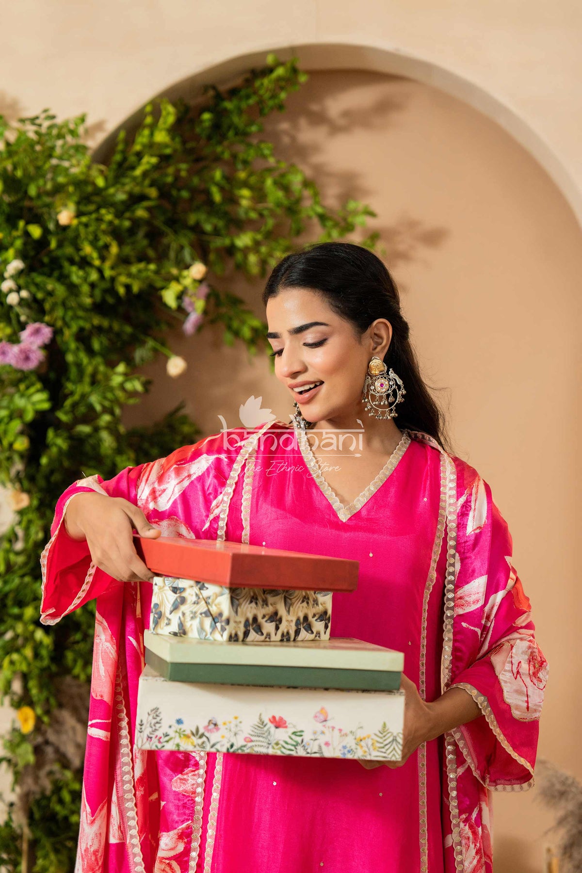 Woman in a pink traditional outfit holding books with a decorative background