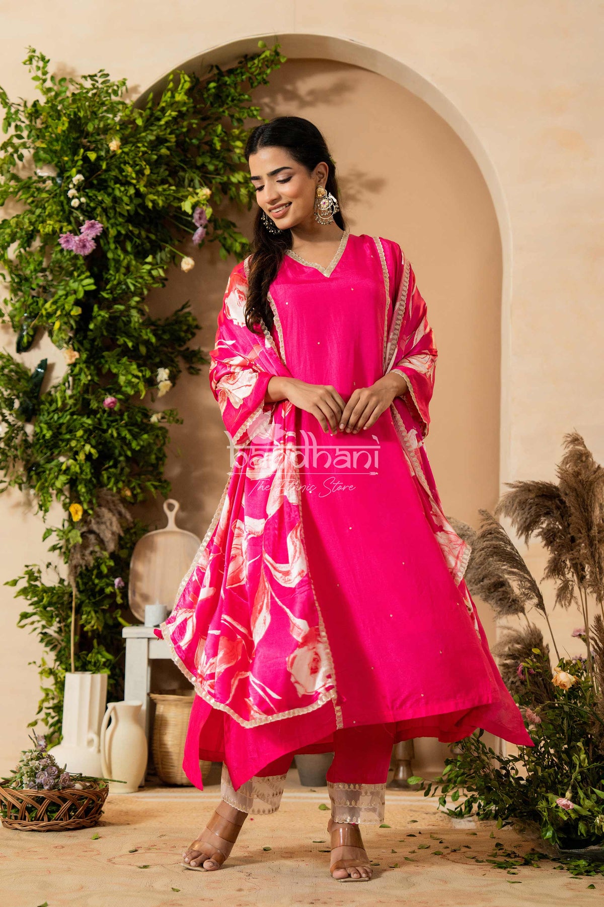 Woman in a bright pink traditional outfit with floral patterns standing in a decorative setting.