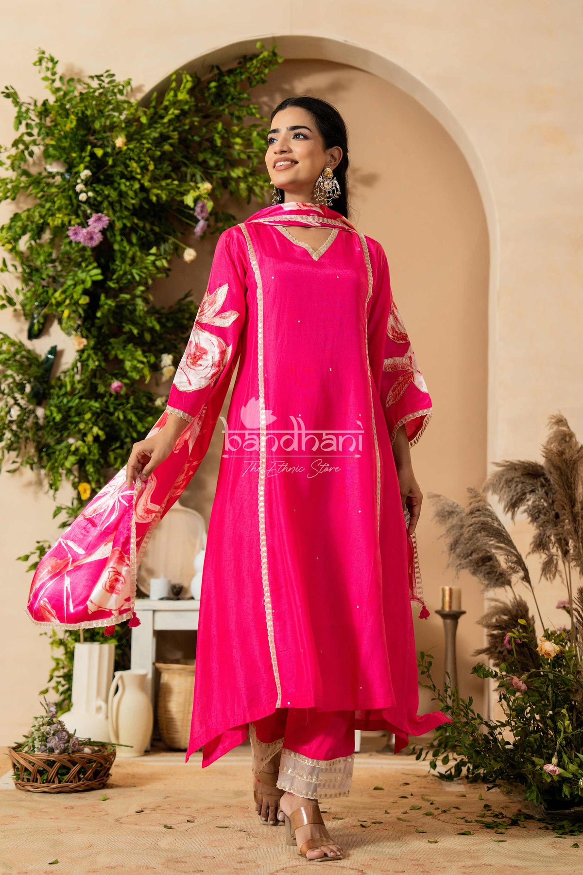 Woman in a bright pink traditional outfit with white patterns, standing in a decorative setting.