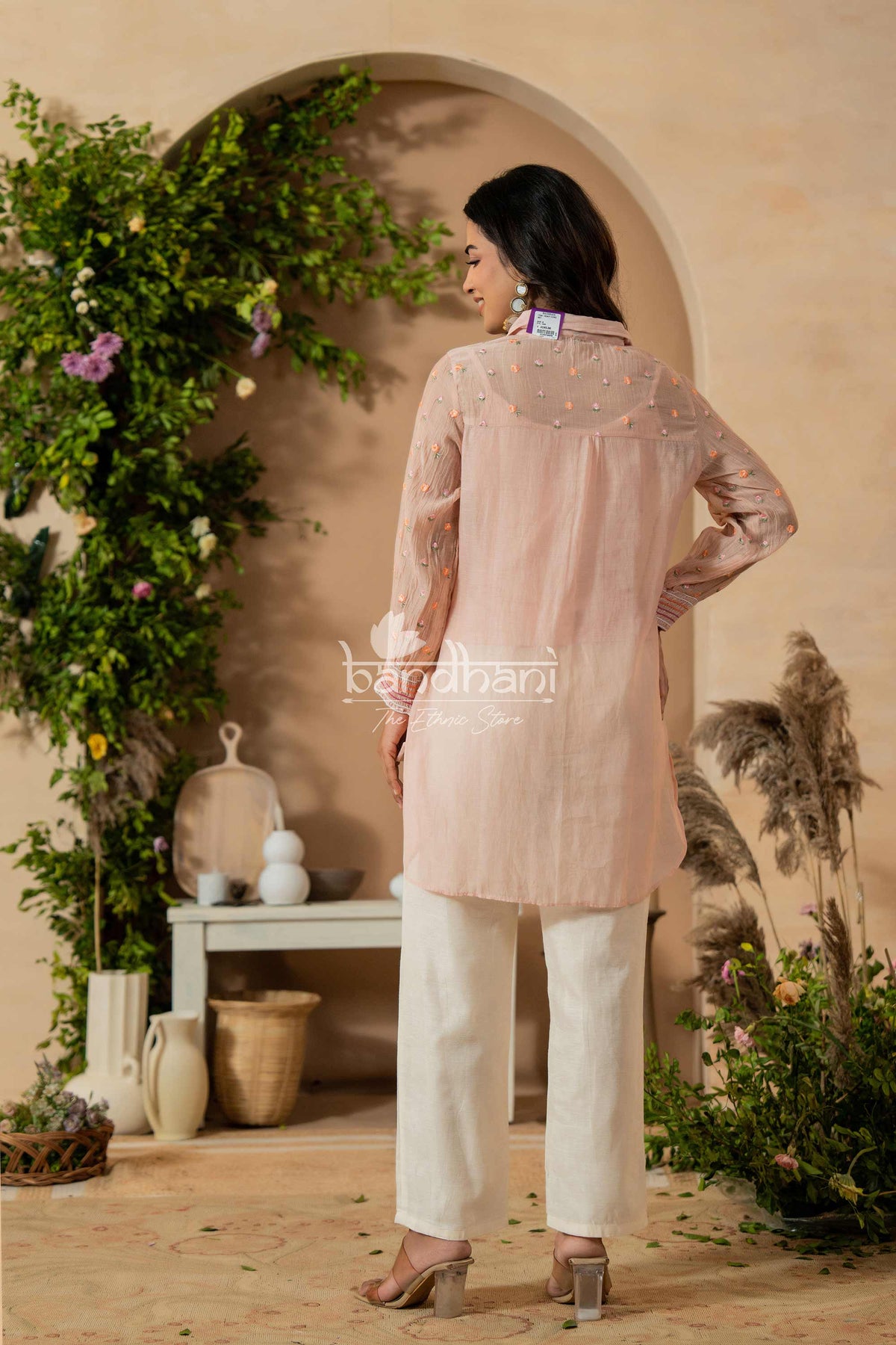 Woman wearing a light pink kurta with white pants in a decorative indoor setting.