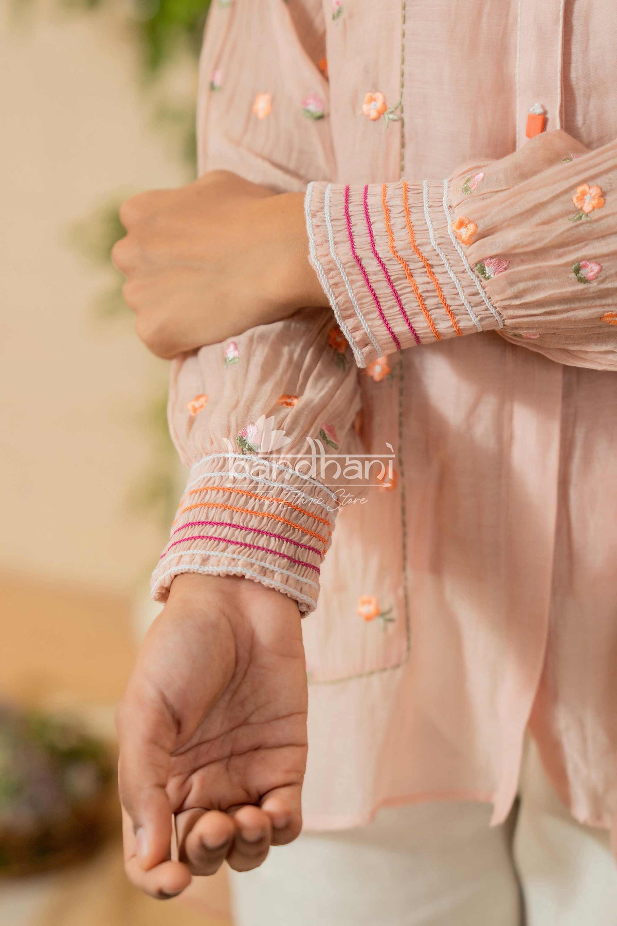 Close-up of a peach-colored embroidered shirt with colorful cuffs, featuring the brand 'Bhandari'.