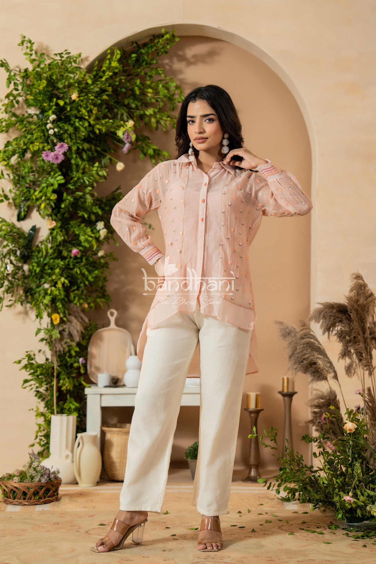 Woman wearing a pink traditional outfit with white pants in a decorated indoor setting.