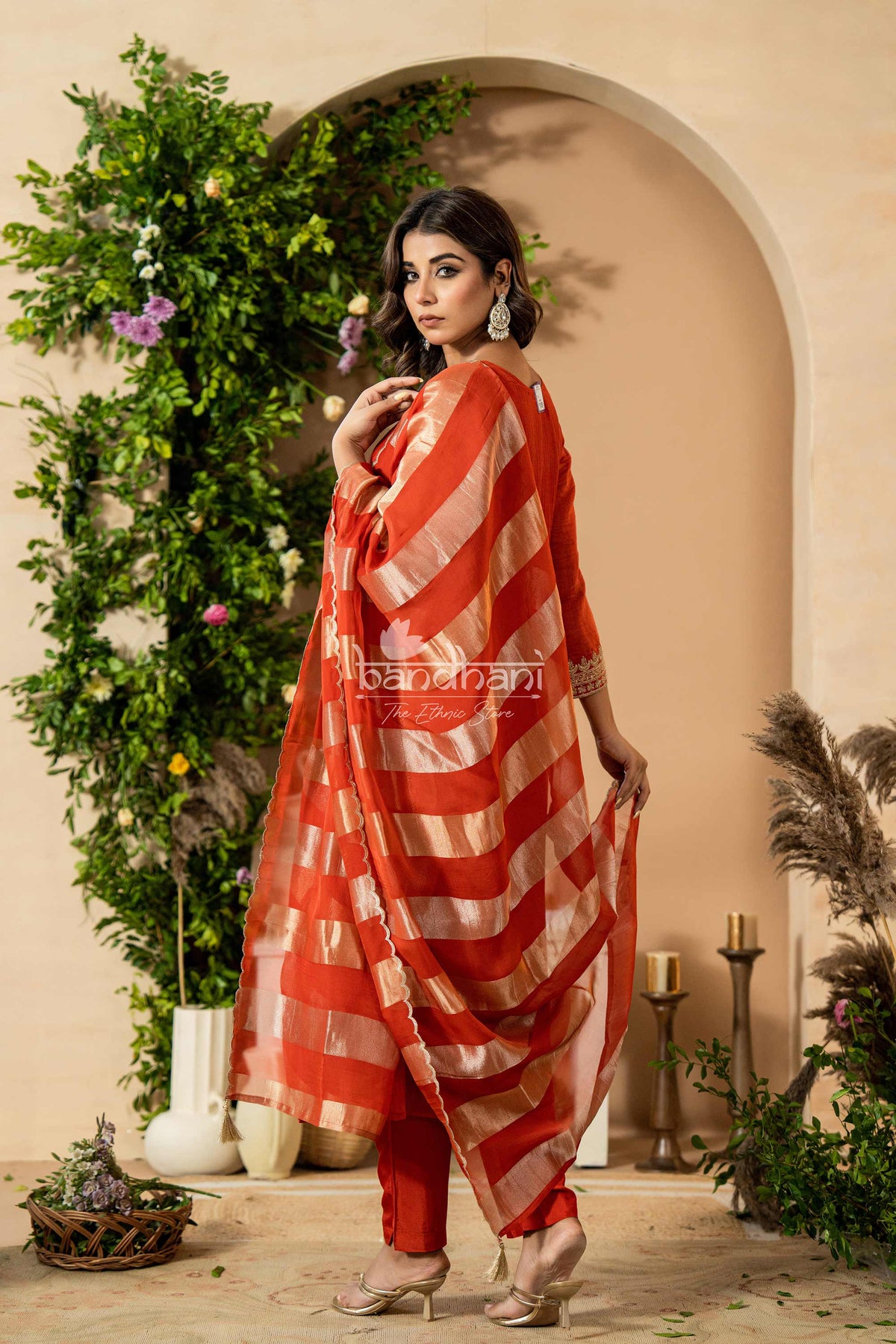 Woman in a red and white striped saree standing in a decorated indoor setting with plants and candles.