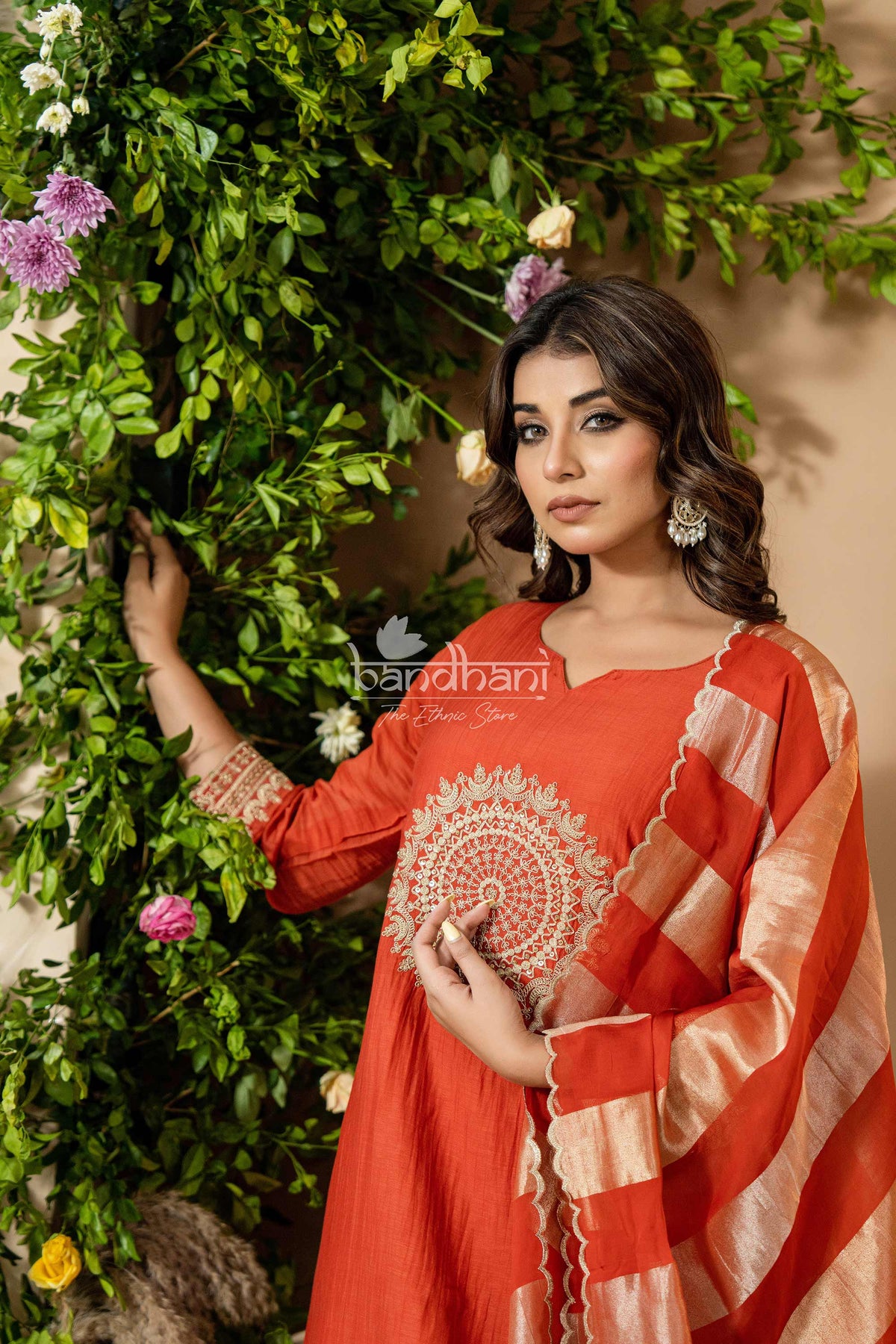 Woman in a red traditional outfit with gold details against a green leafy background