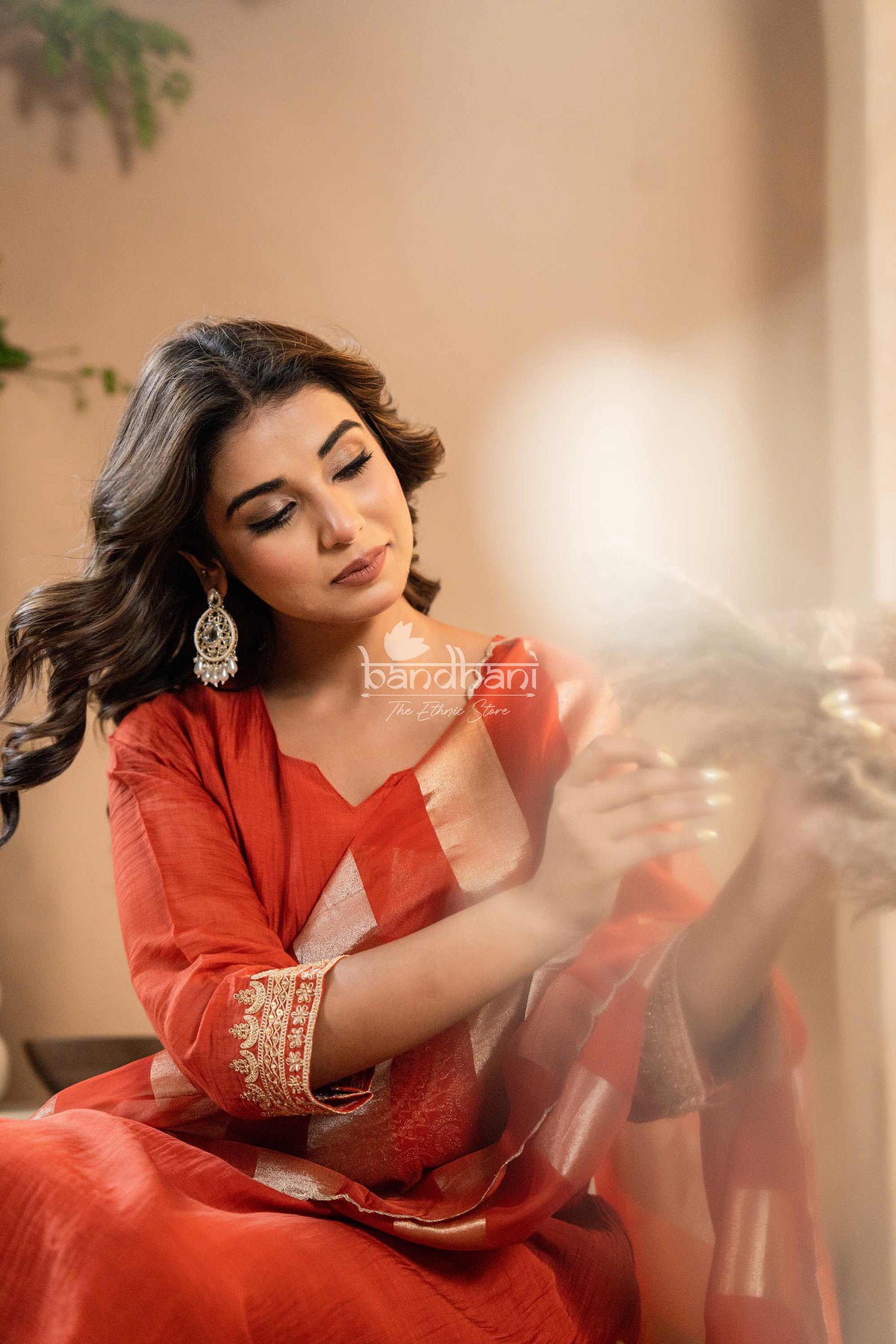 Woman in a red traditional outfit with intricate designs, sitting indoors.
