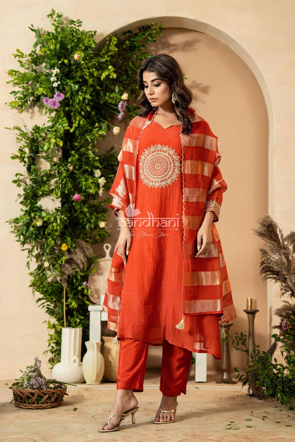 Woman wearing a red traditional outfit with intricate patterns in a decorated indoor setting.