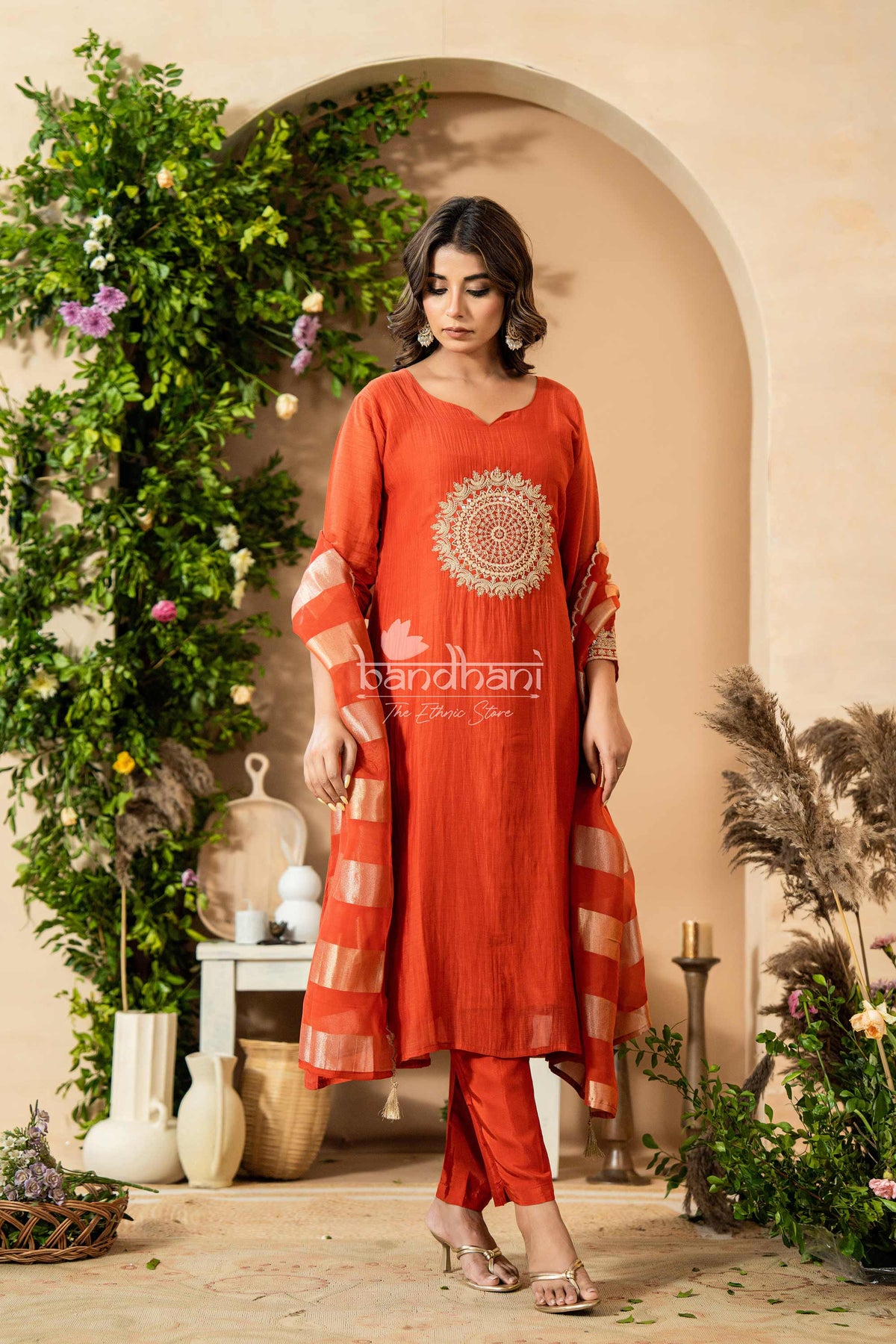 Woman wearing a red traditional outfit with intricate patterns in a decorated indoor setting.