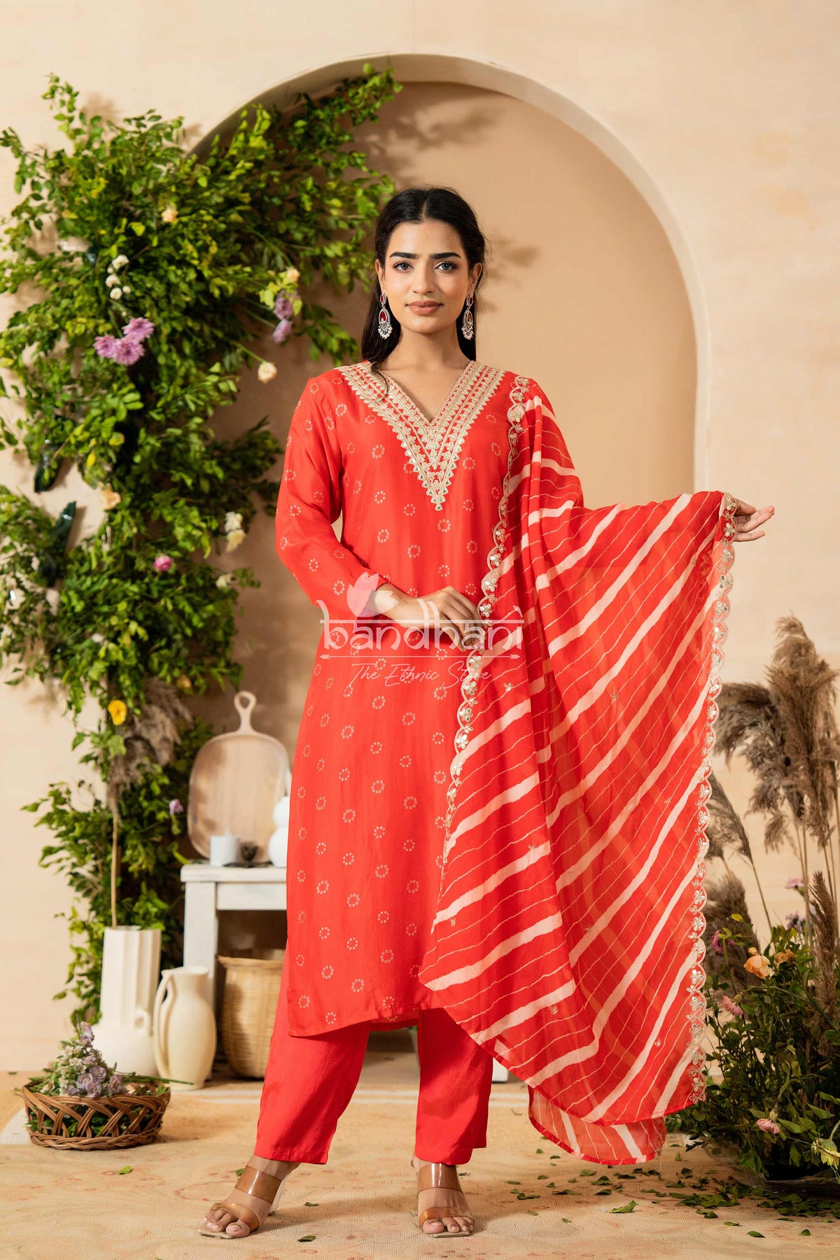 Woman in a red traditional outfit with a matching dupatta, standing in a decorated indoor setting.