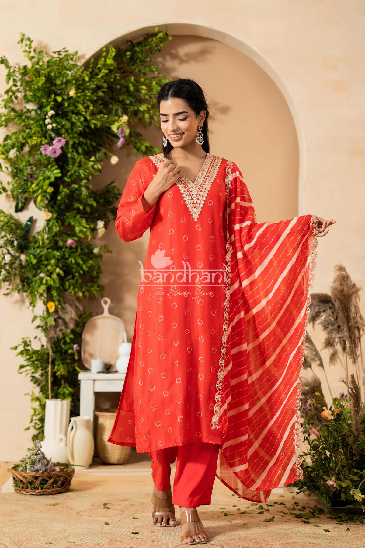 Woman in a red traditional outfit with a dupatta, standing in a decorative indoor setting.