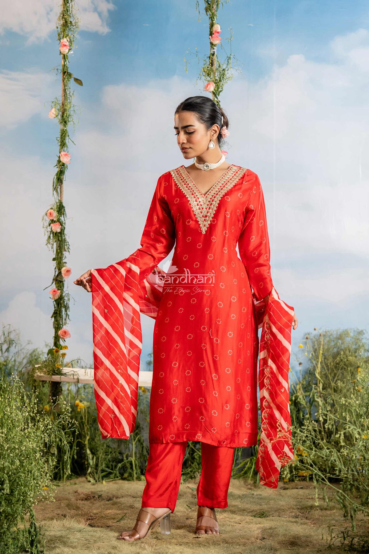 Woman in a red traditional outfit standing outdoors with floral decorations.