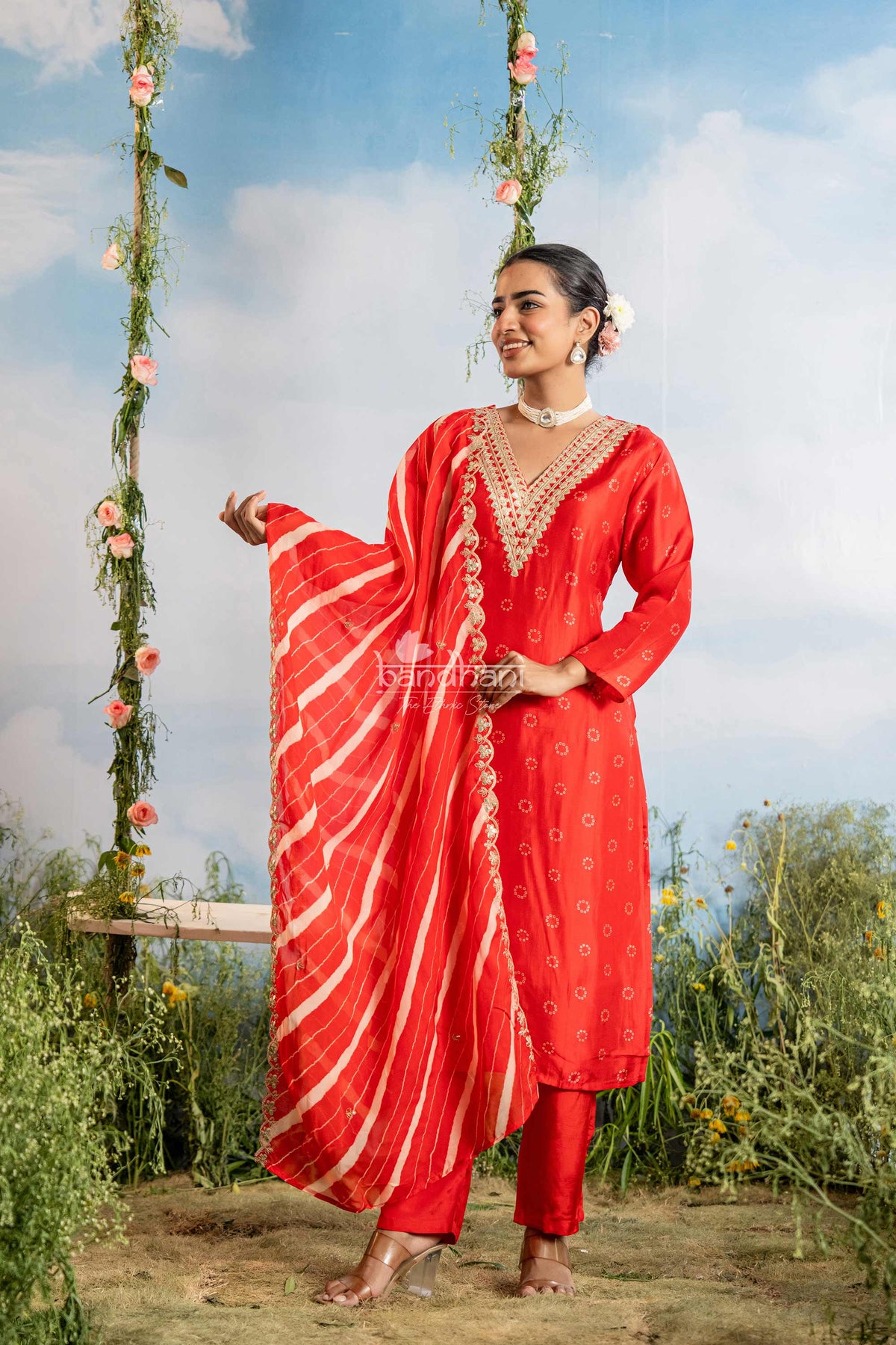 Woman in a red traditional outfit standing outdoors with floral decorations.