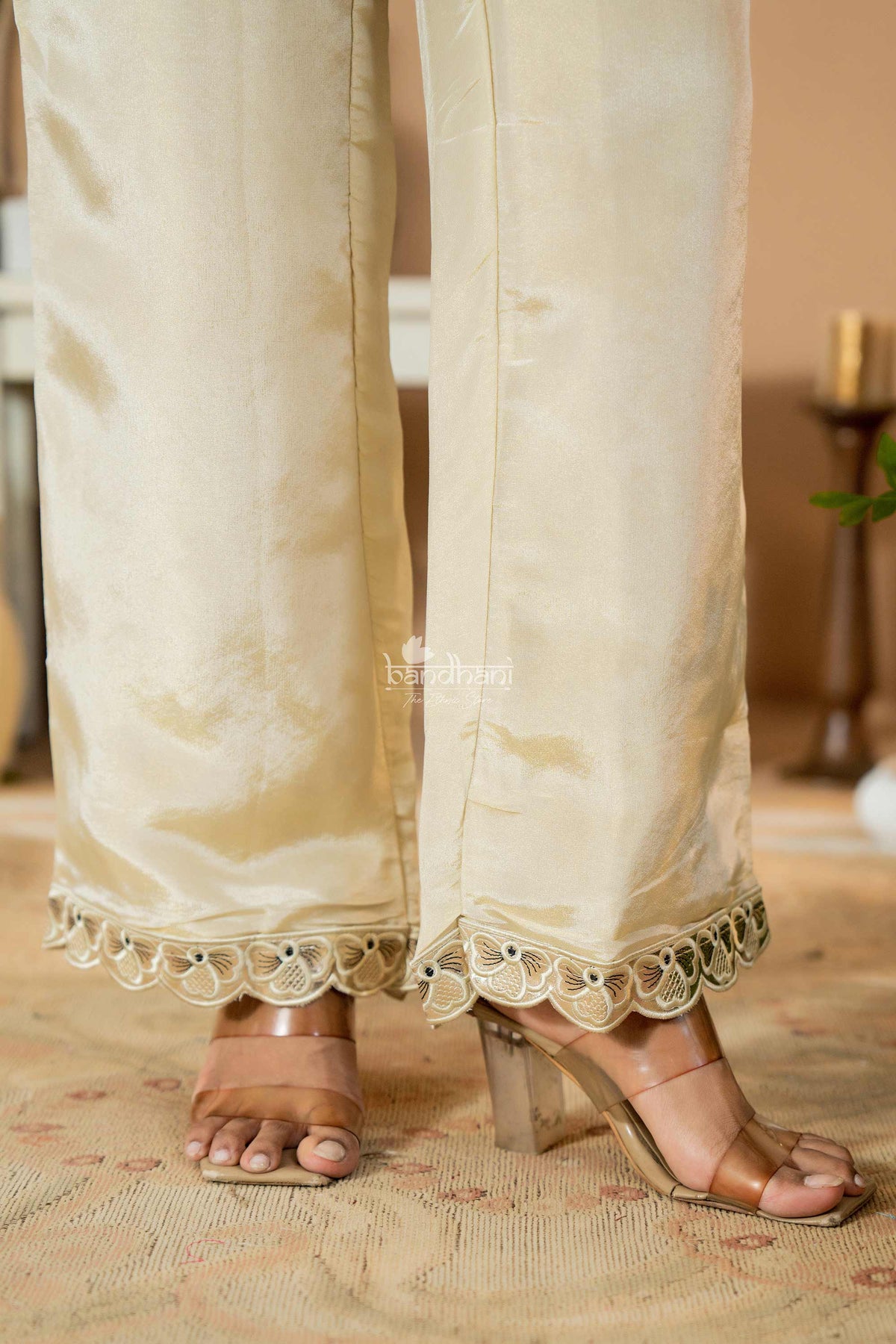 Beige pants with lace trim worn by a person, standing on a patterned rug.