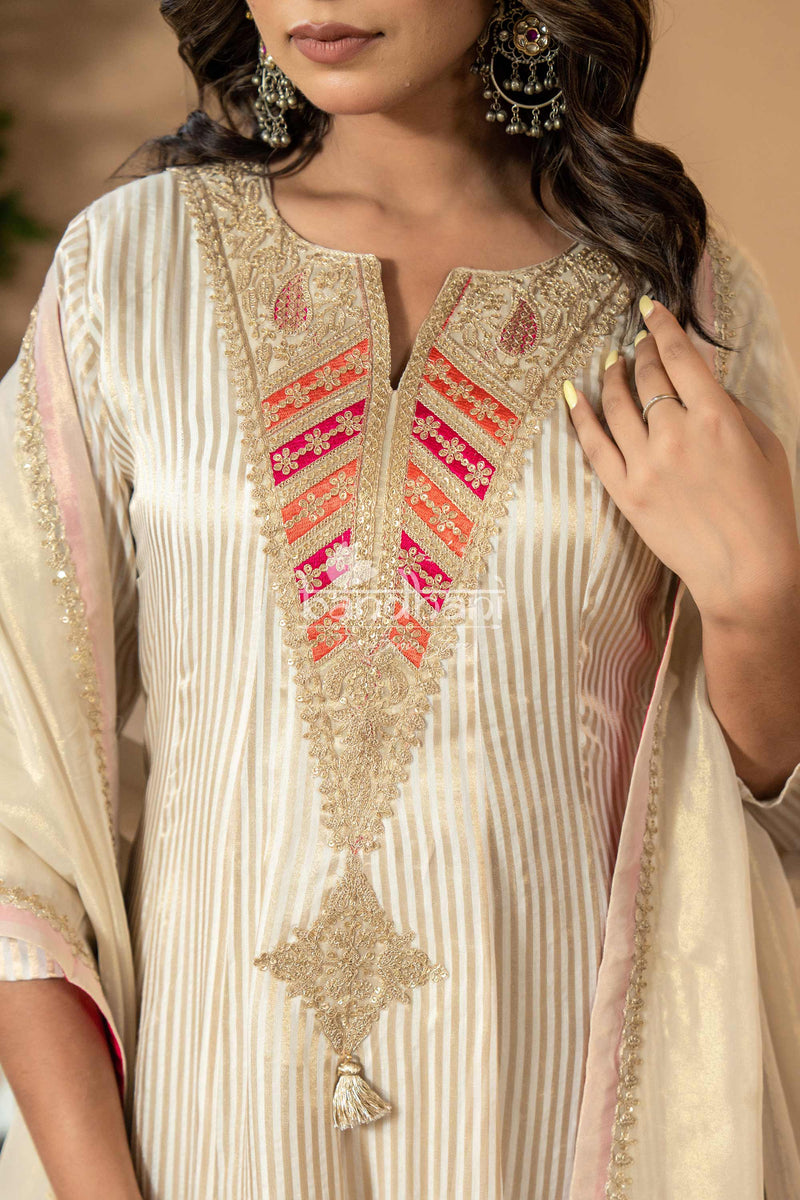 Woman wearing a cream embroidered traditional outfit with intricate designs.