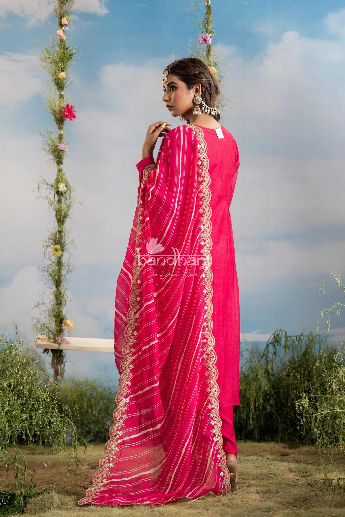 Woman wearing a bright pink saree with gold patterns against a natural background