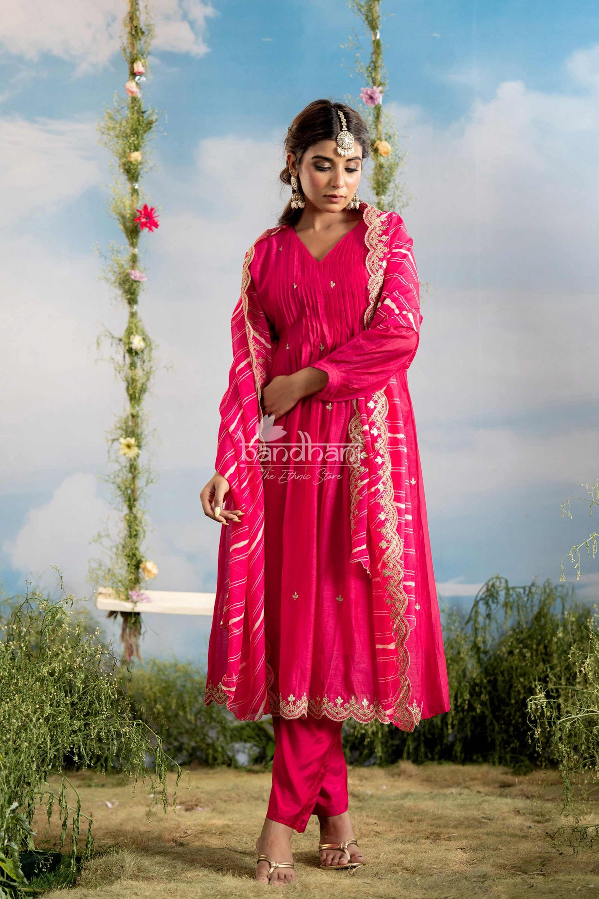 Woman in a bright pink traditional outfit standing outdoors with a scenic background
