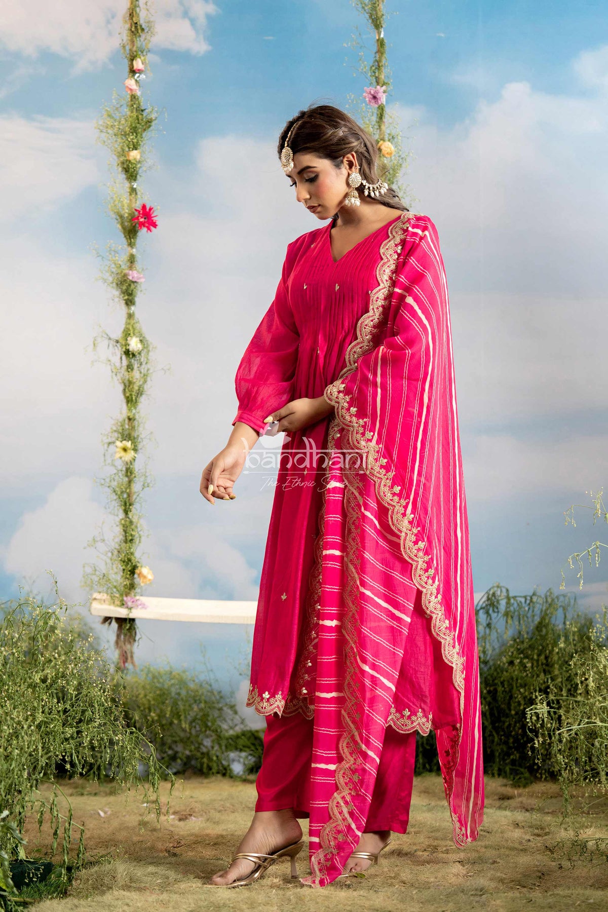 Woman in a bright pink traditional outfit standing on a grassy area with a swing in the background.