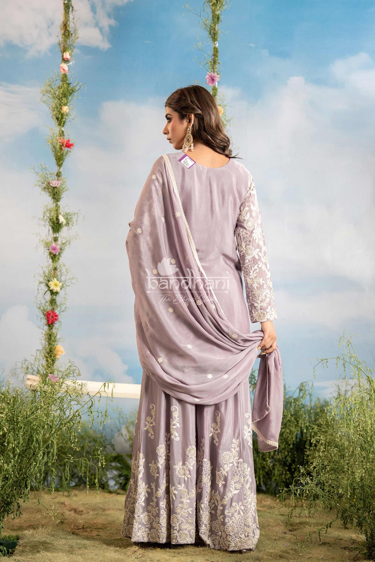 Woman in a lavender saree with floral decorations and a blue sky background