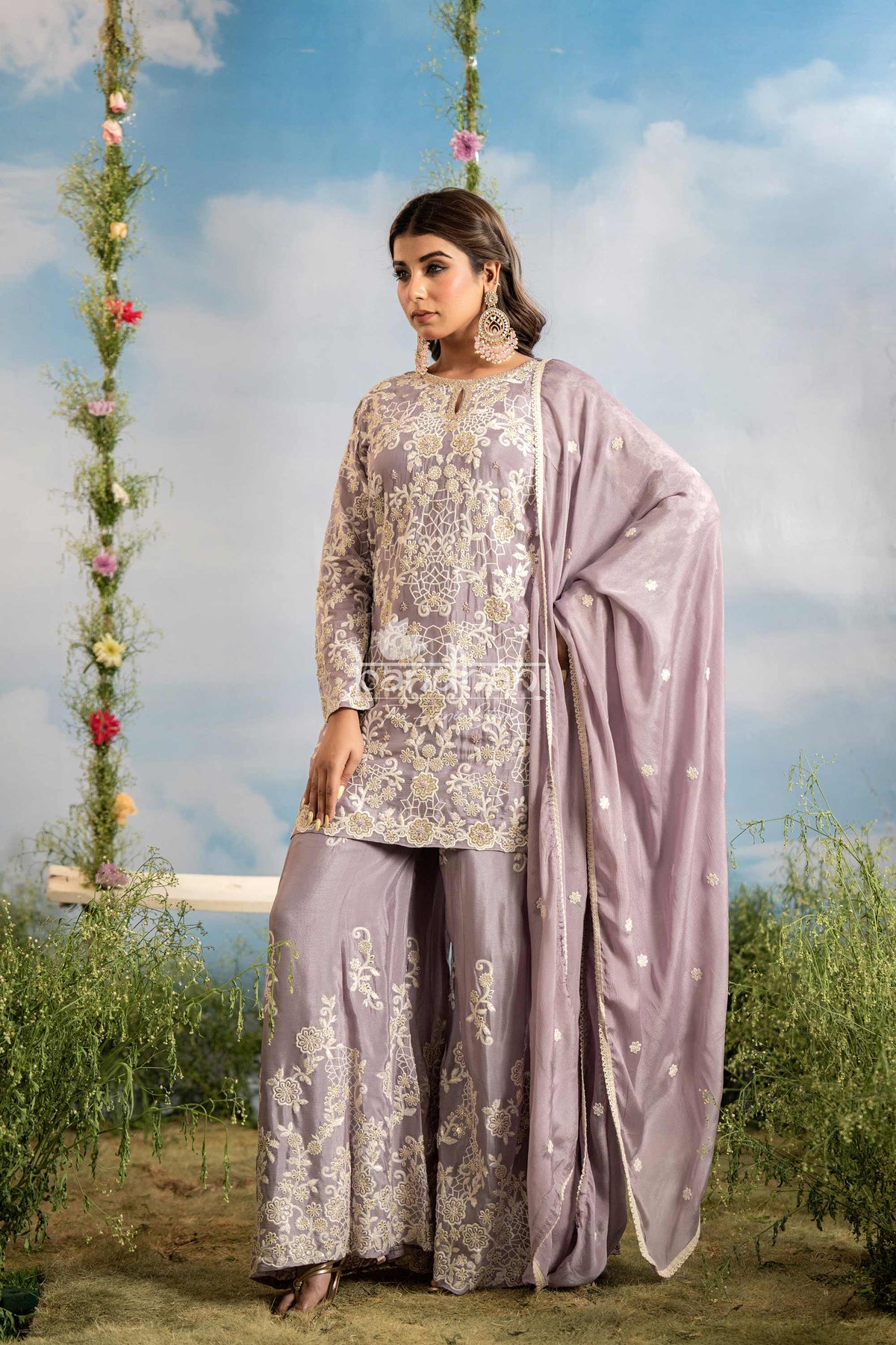Woman in a traditional outfit with floral patterns standing outdoors against a blue sky.