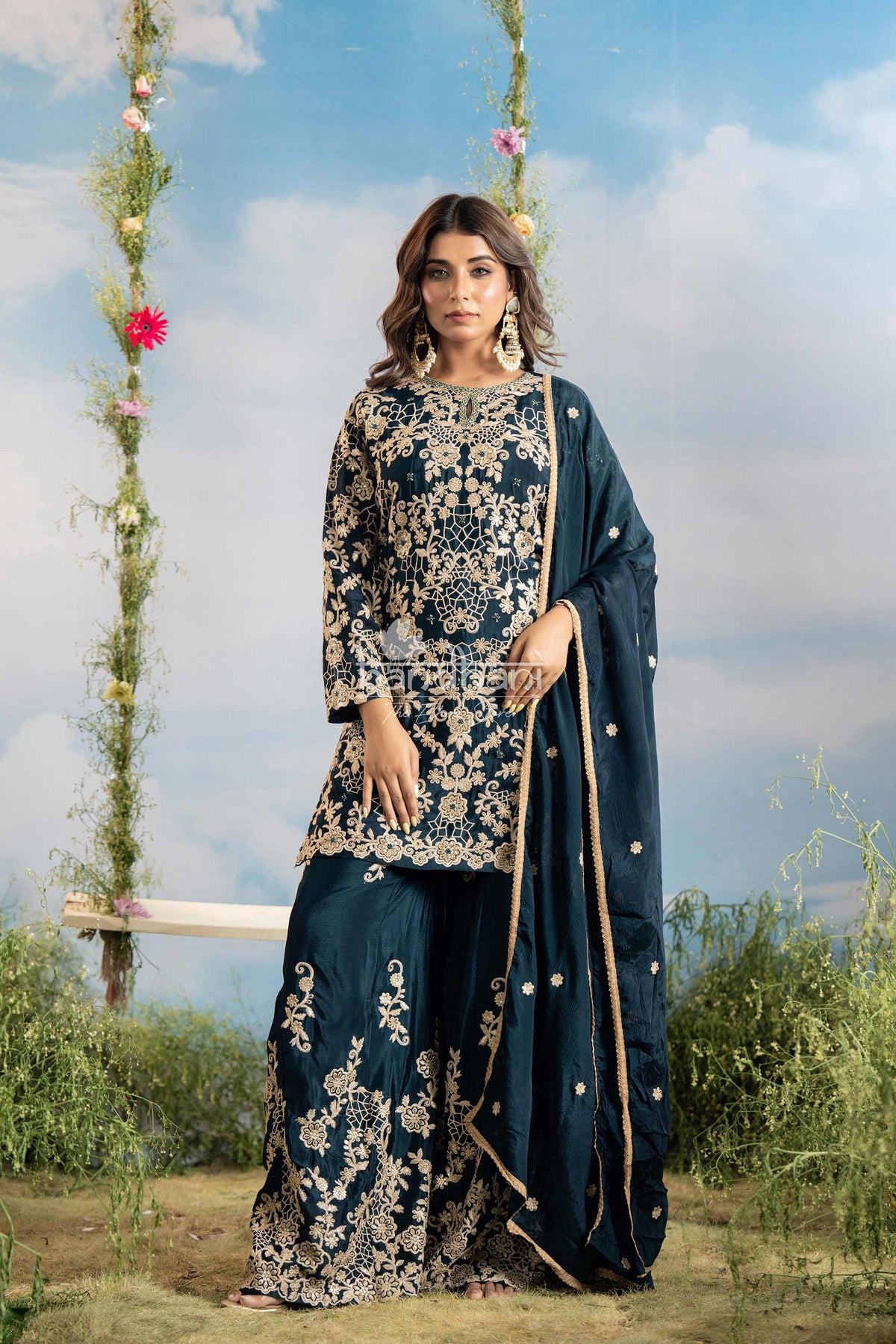 Woman in a traditional embroidered outfit standing outdoors with a swing and flowers in the background