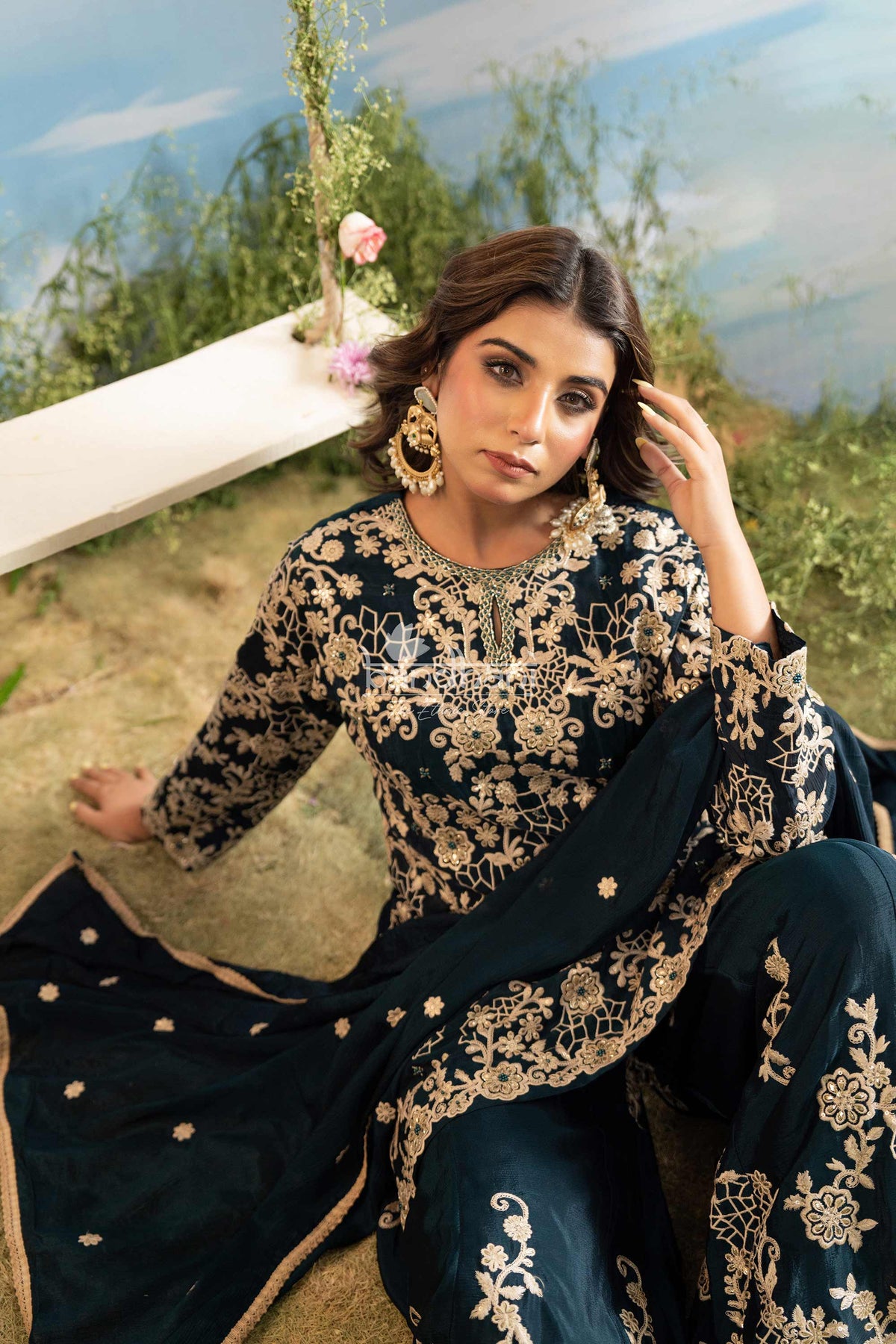 Woman in a navy blue and gold embroidered traditional outfit sitting outdoors.
