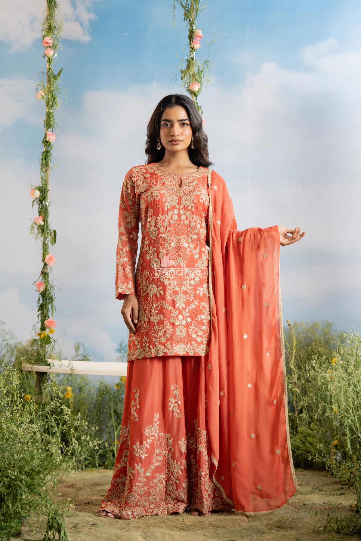 Woman in a traditional outfit with floral patterns standing outdoors against a blue sky.