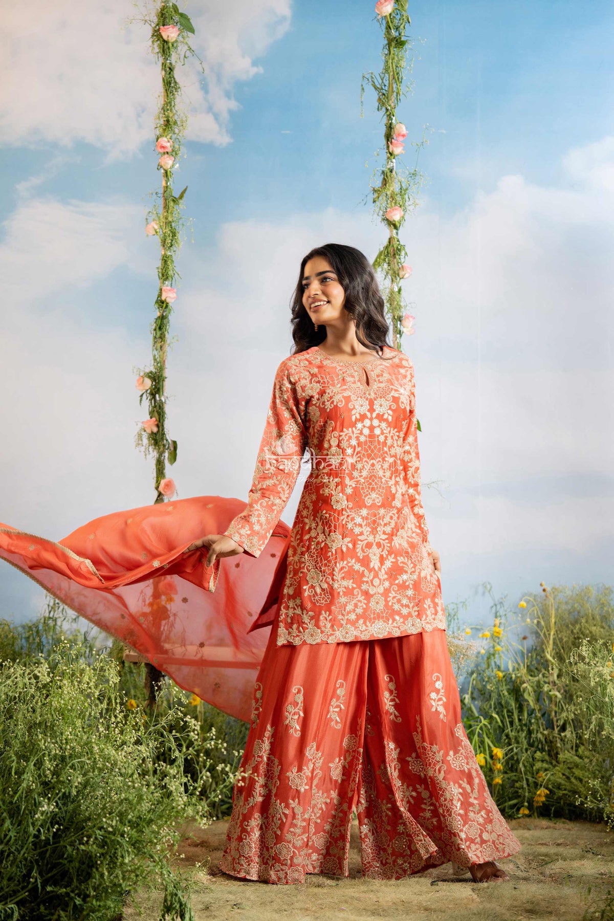 Woman in a traditional outfit standing outdoors with a floral swing in the background