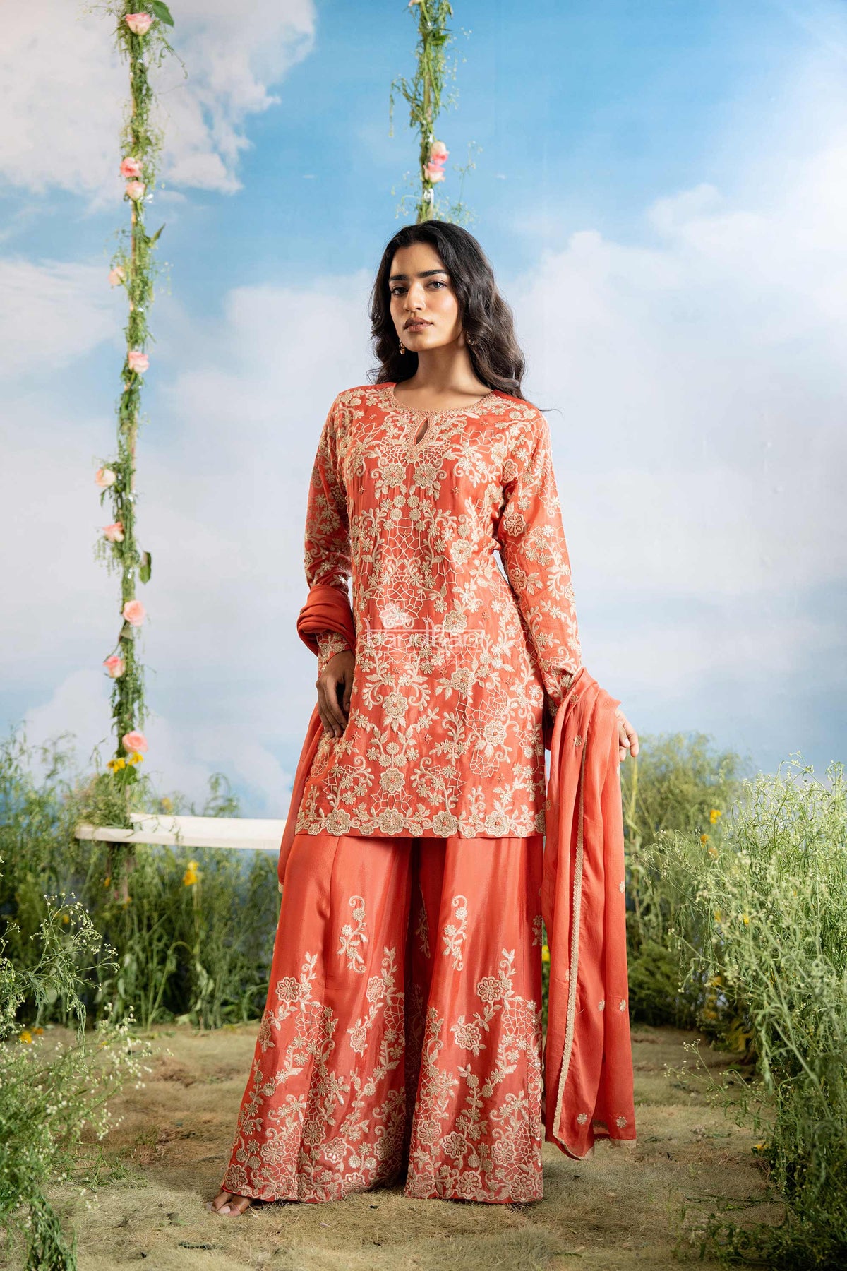 Woman in a floral dress standing outdoors with a swing and blue sky in the background