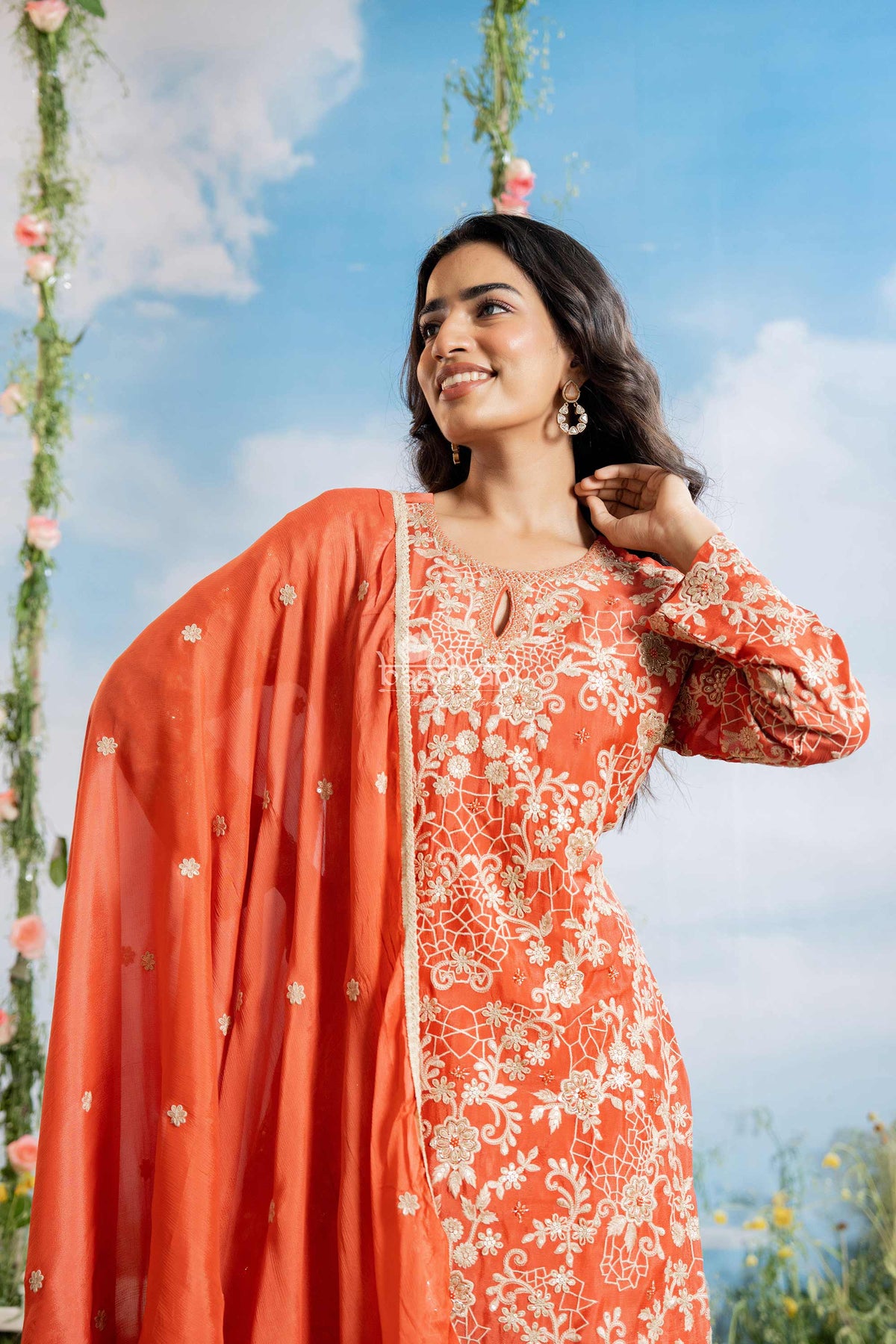 Woman in an orange traditional outfit with floral patterns against a blue sky.